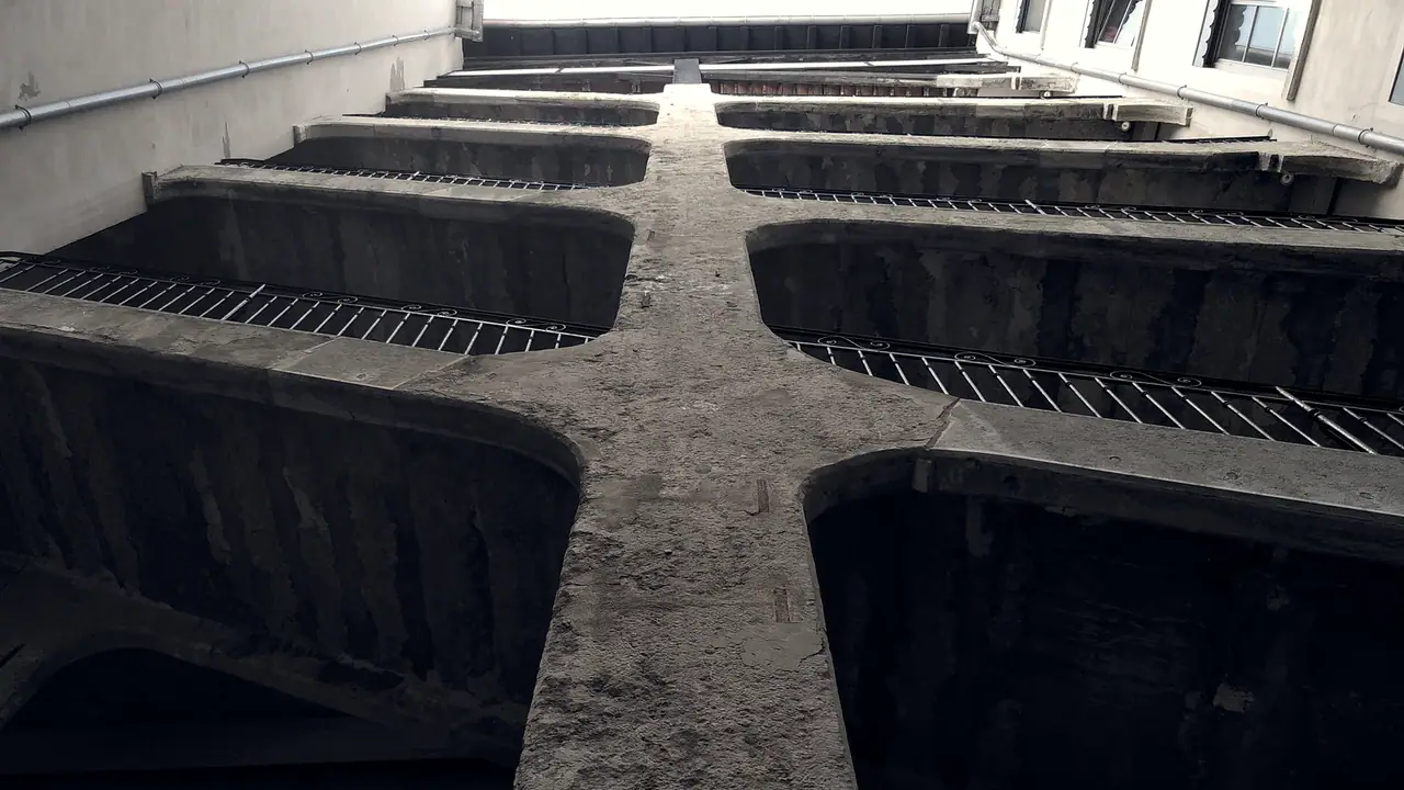 Escalier extérieur d'une cour d'immeuble vu d'en dessous : des volées massives se croisent autour d'un pilier central, bordées de garde-corps en fer forgé.