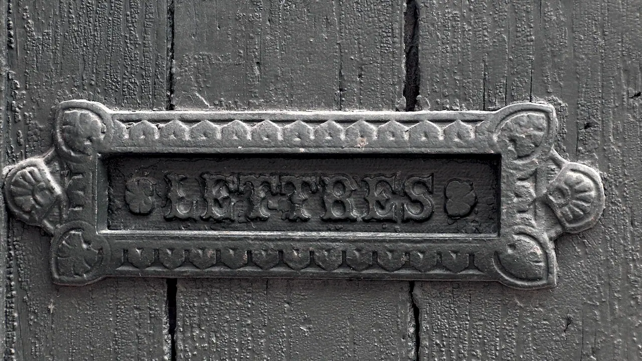 Fente de boîte aux lettres en fonte marquée LETTRES, vissée sur une vieille porte de bois peinte en gris.