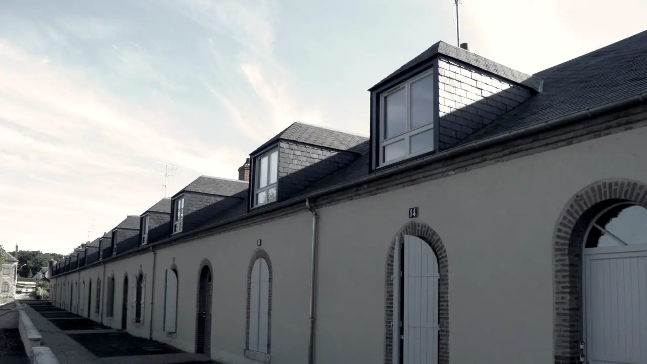 Longue rangée de logements identiques sous un même toit continu, leurs portes cintrées alignées le long de la rue.