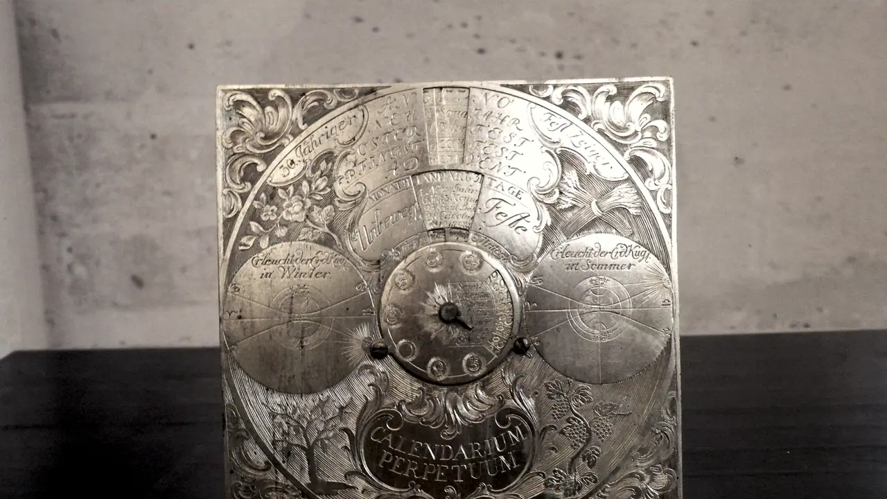 Calendrier perpétuel gravé sur une plaque de métal, avec des cadrans mobiles pour les mois, les jours et les fêtes, posé sur une table.