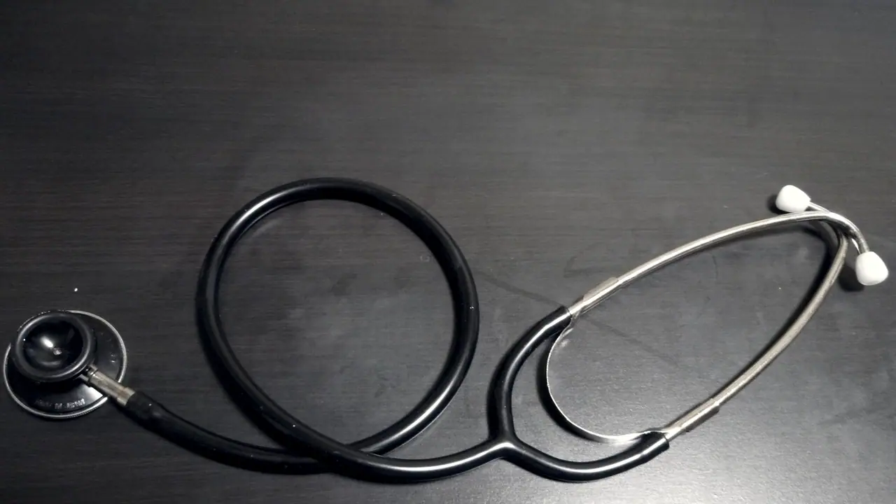 Stéthoscope posé sur une table de bois sombre, sa tubulure noire bouclée entre le pavillon à gauche et les embouts d'écoute à droite.