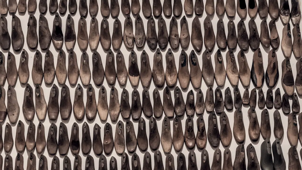 Centaines de formes à chaussures en bois accrochées par rangées serrées sur un mur clair, chacune taillée pour une pointure différente.