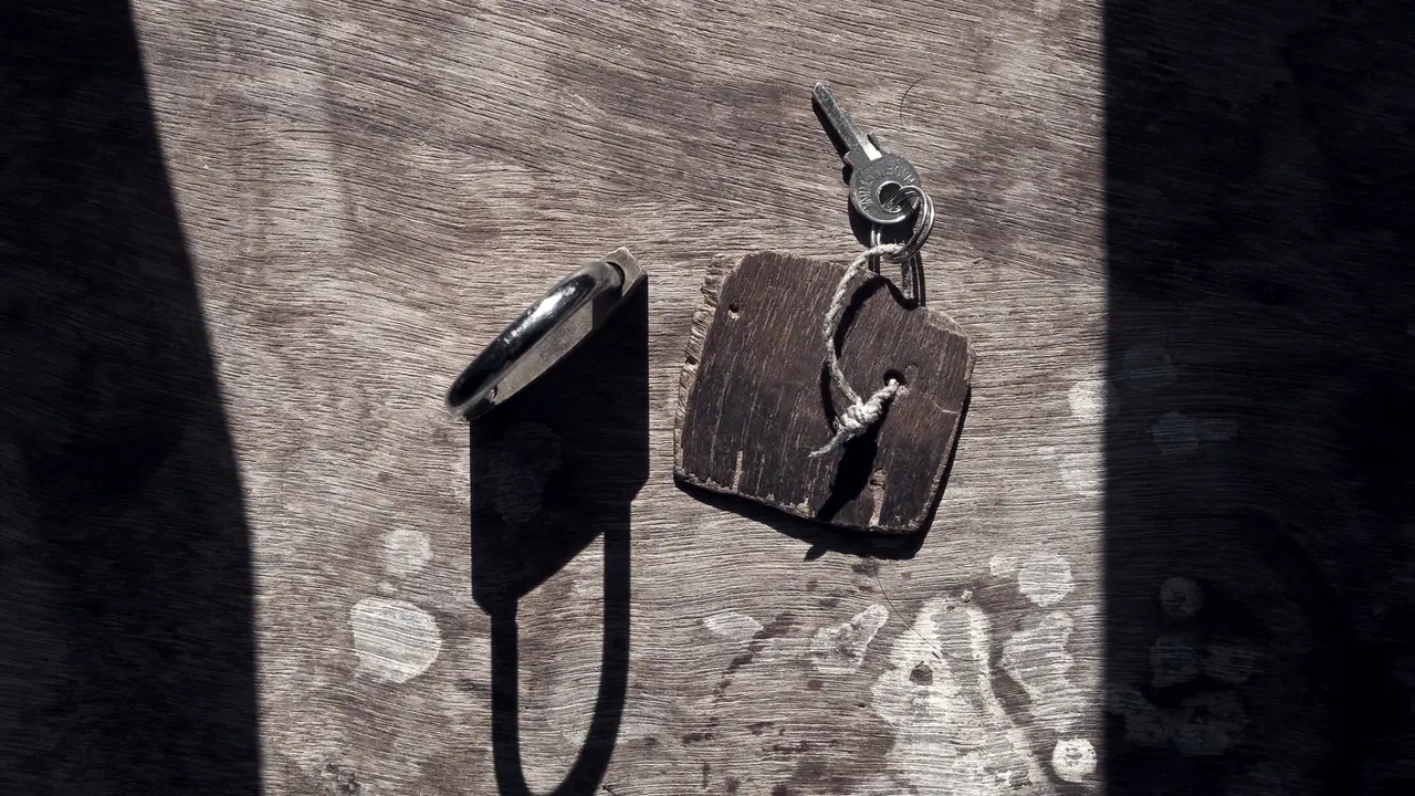 Clé accrochée à un jeton de bois, posée près d'un cadenas, sur des planches usées par les intempéries.