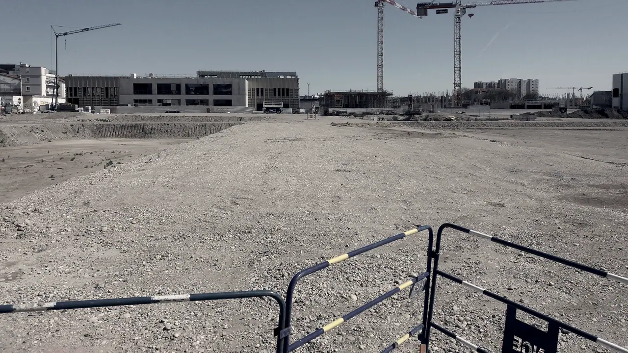 Terrain de chantier terrassé devant des immeubles en construction, avec ses grues et les barrières qui ferment l'emprise.