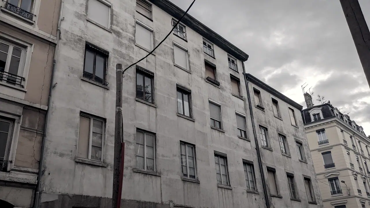 Immeubles d'habitation lyonnais serrés les uns contre les autres le long d'une rue, façades claires et fenêtres régulières.