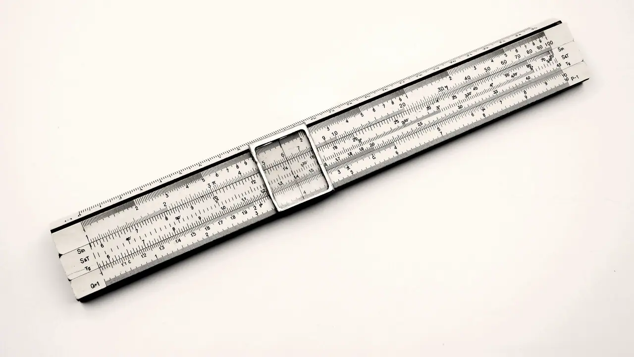 Règle à calcul ancienne posée en diagonale sur un fond blanc, avec son curseur de verre au centre et ses échelles graduées sur toute la longueur.
