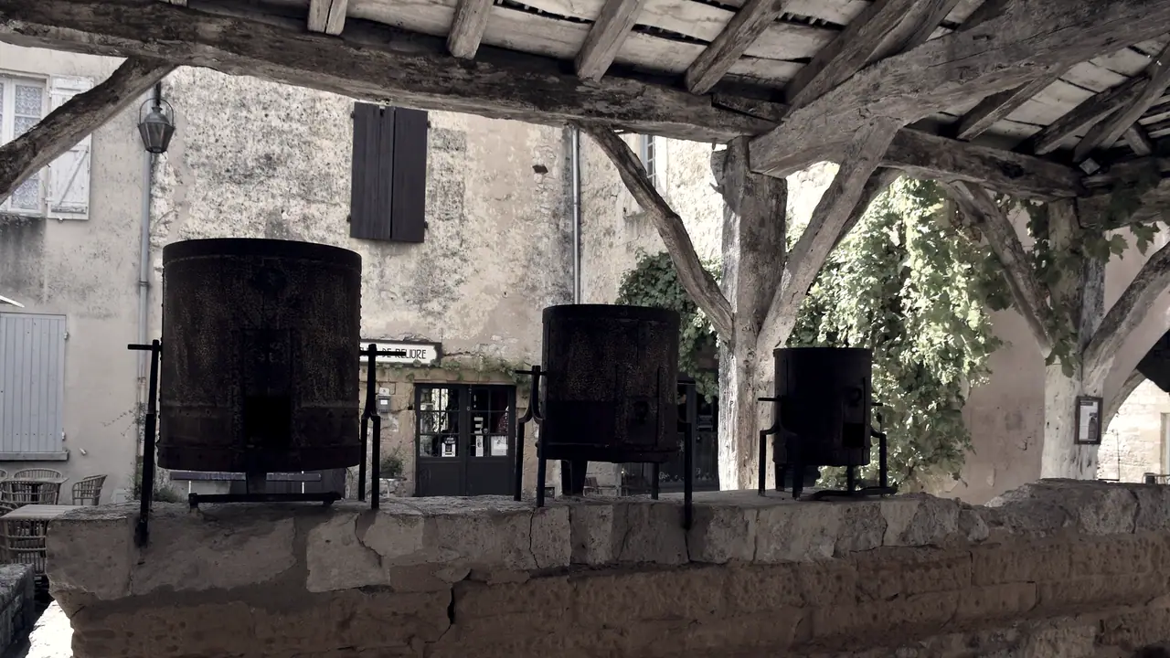 Trois mesures à grain en fer, de tailles décroissantes, alignées sur le muret de pierre d'une halle ancienne, sous sa charpente de bois.