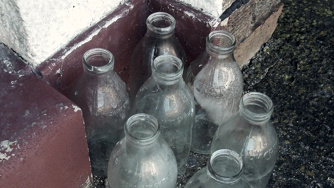 Bouteilles de lait en verre, vides, regroupées dans l'angle d'un seuil de maison en attendant d'être rendues au laitier.