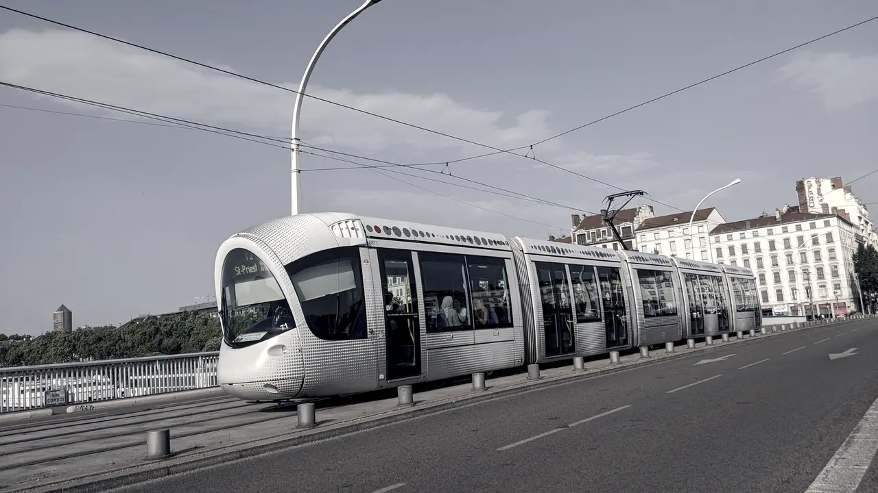 Rame de tramway qui traverse un pont urbain sous ses caténaires, avec les immeubles de l'autre rive.
