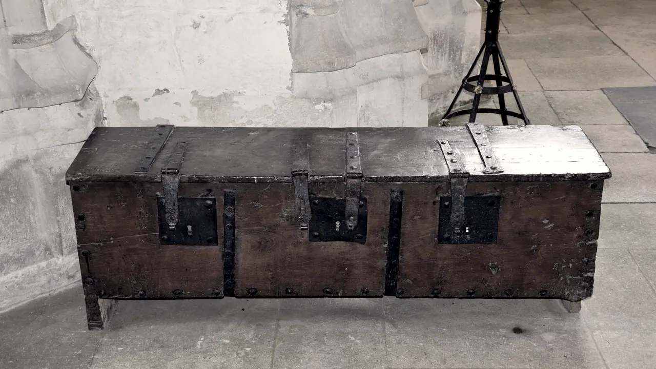 Coffre de paroisse ancien en bois sombre, fermé par trois serrures à moraillon alignées sur sa face, posé sur le dallage de pierre d'une église.