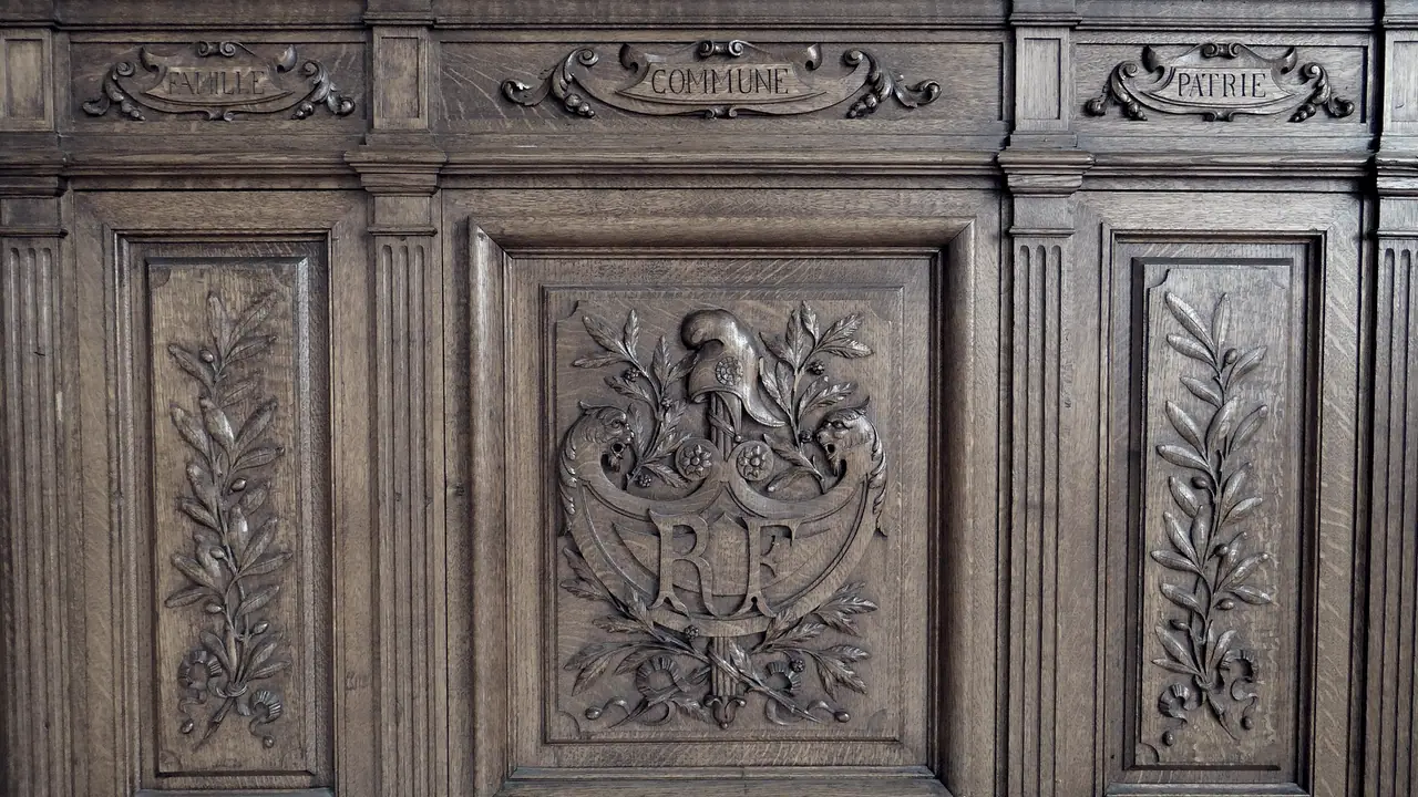 Lambris de chêne sculpté d'une salle des mariages, avec les mots Famille, Commune et Patrie au-dessus d'un médaillon aux initiales RF entouré de feuillages.