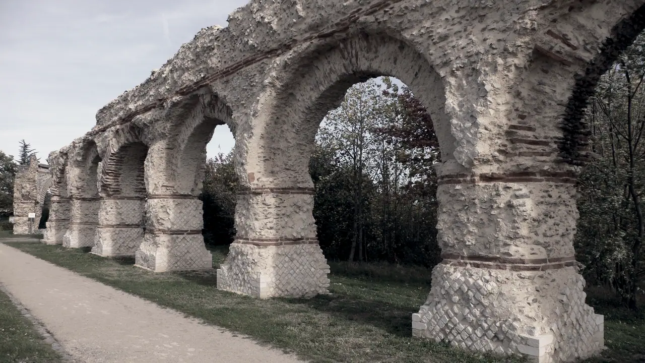 File d'arches de pierre d'un aqueduc antique qui s'éloigne le long d'un chemin, entre l'herbe et les arbres.