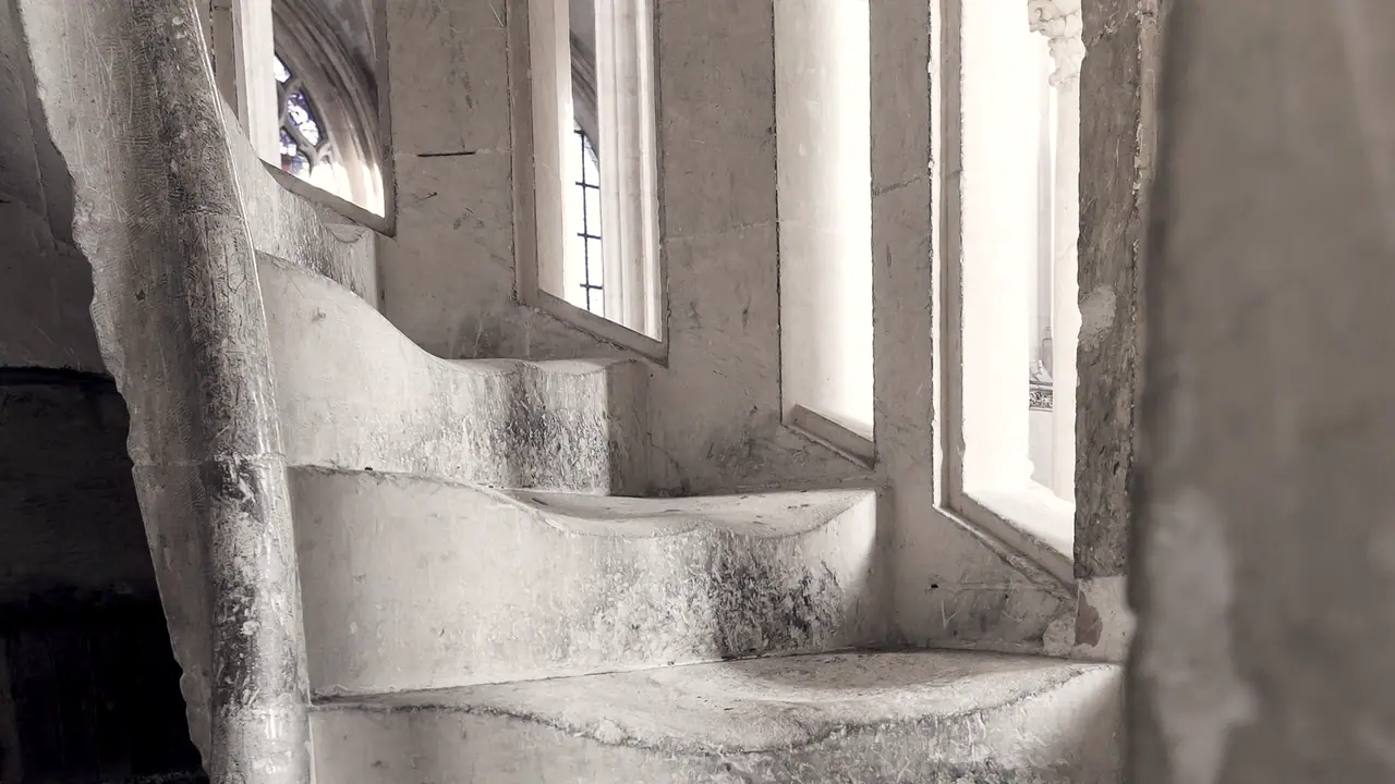 Marches de pierre usées d'un escalier à vis, devant de hautes fenêtres étroites vitrées dans un édifice ancien.