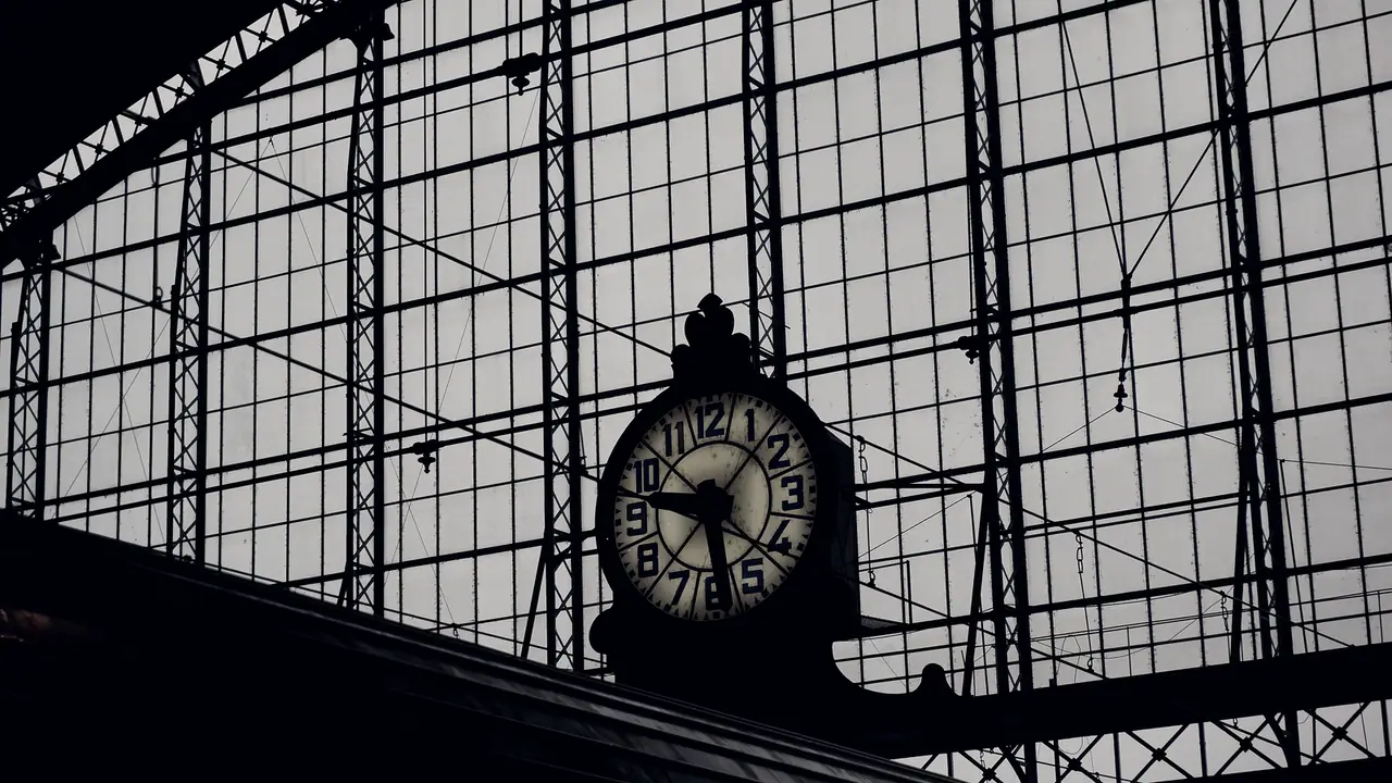 Horloge suspendue sous la verrière d'une gare, son cadran chiffré détaché contre les armatures du toit vitré.