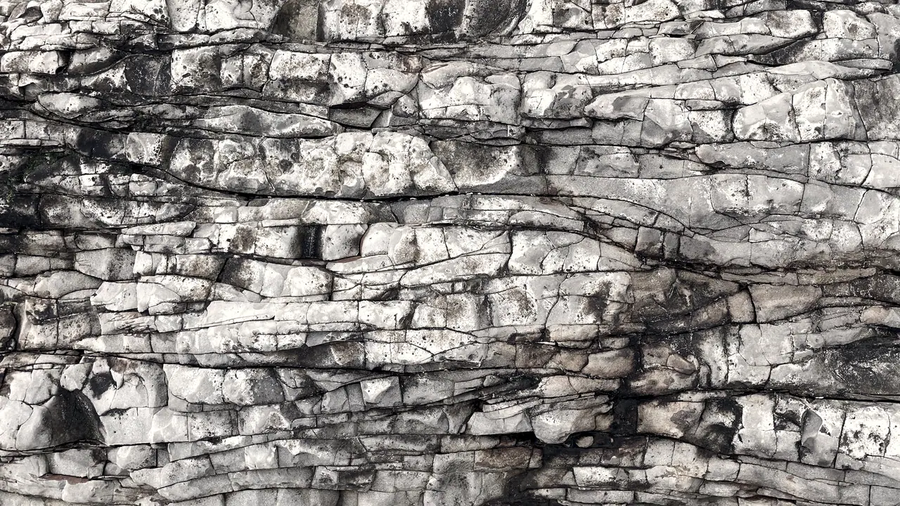 Paroi rocheuse naturelle en strates horizontales : des dizaines de lits de roche fissurés, empilés les uns sur les autres.