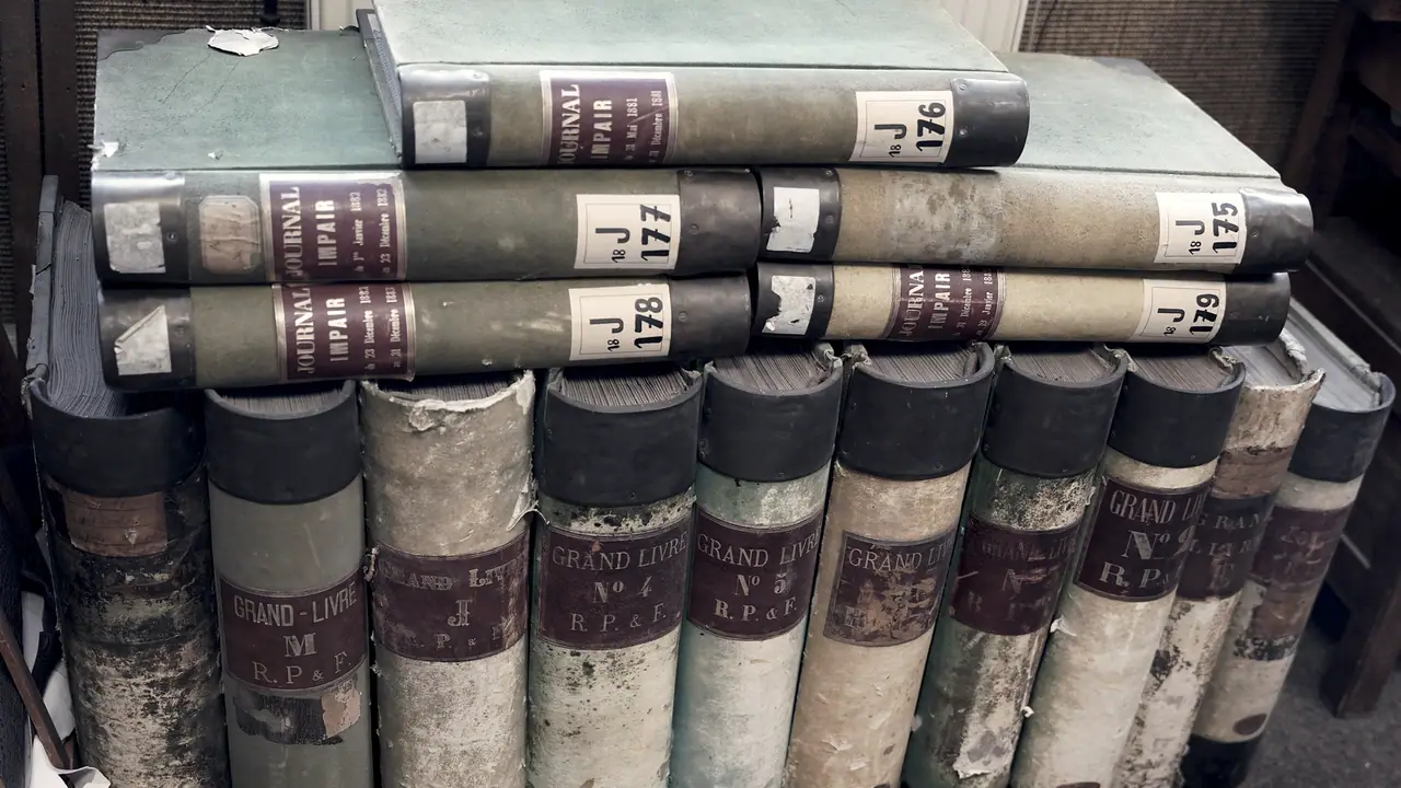 Registres comptables anciens empilés et alignés, avec des étiquettes de grand livre et de journal sur leurs dos.