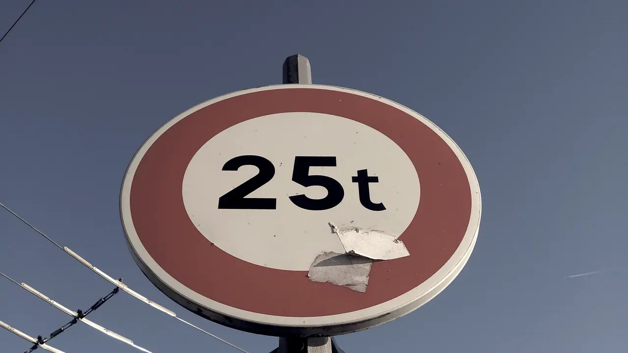 Panneau rond interdisant le passage aux véhicules de plus de 25 tonnes, vu en contre-plongée sur un ciel bleu, avec des câbles tendus au-dessus de la rue.