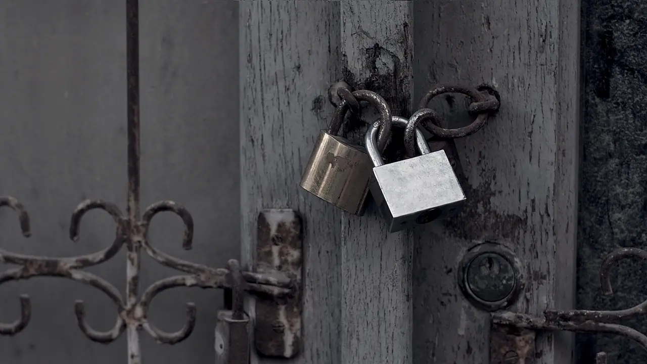 Deux cadenas, l'un en laiton et l'autre en acier, accrochés ensemble entre deux anneaux rouillés sur le montant d'une vieille porte de bois.