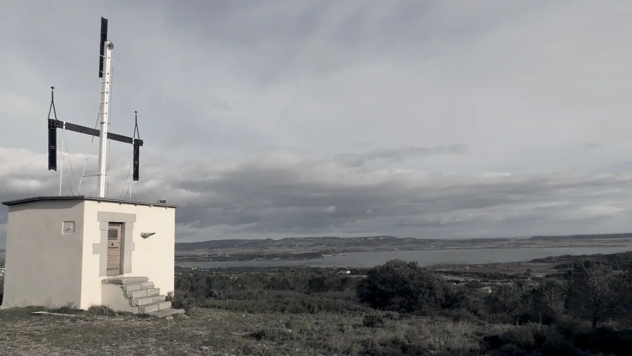 Télégraphe Chappe dressé sur le toit d'une petite tour blanche, ses bras de signaux tournés vers un étang et une plaine qui s'étendent au loin.
