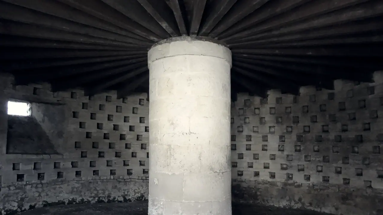 Intérieur d'un colombier ancien : autour d'un pilier de pierre, les niches des pigeons s'alignent sur le mur en rangées et en colonnes régulières.