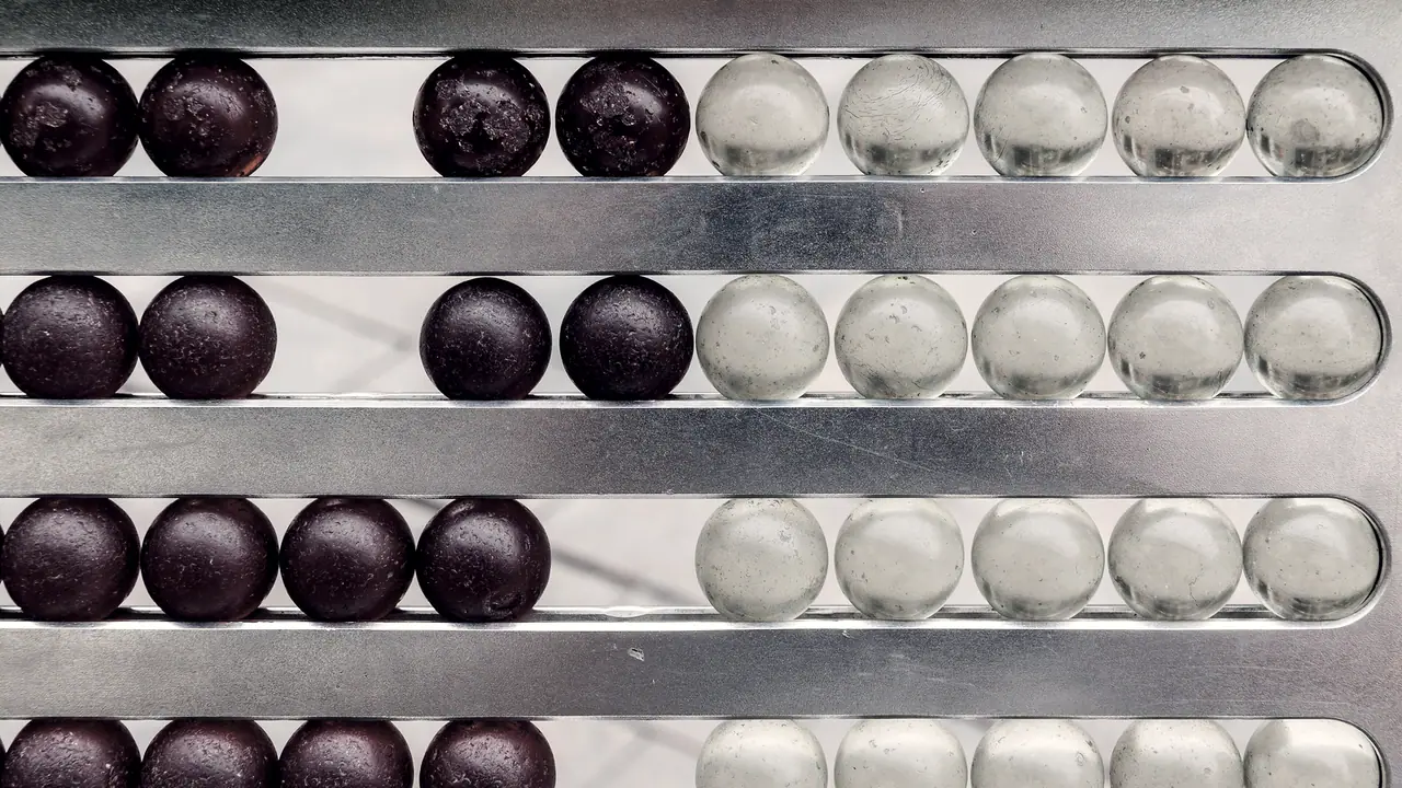 Boulier de métal vu de face : sur chaque rangée, des billes sombres sont poussées à gauche et des billes de verre clair restent groupées à droite.