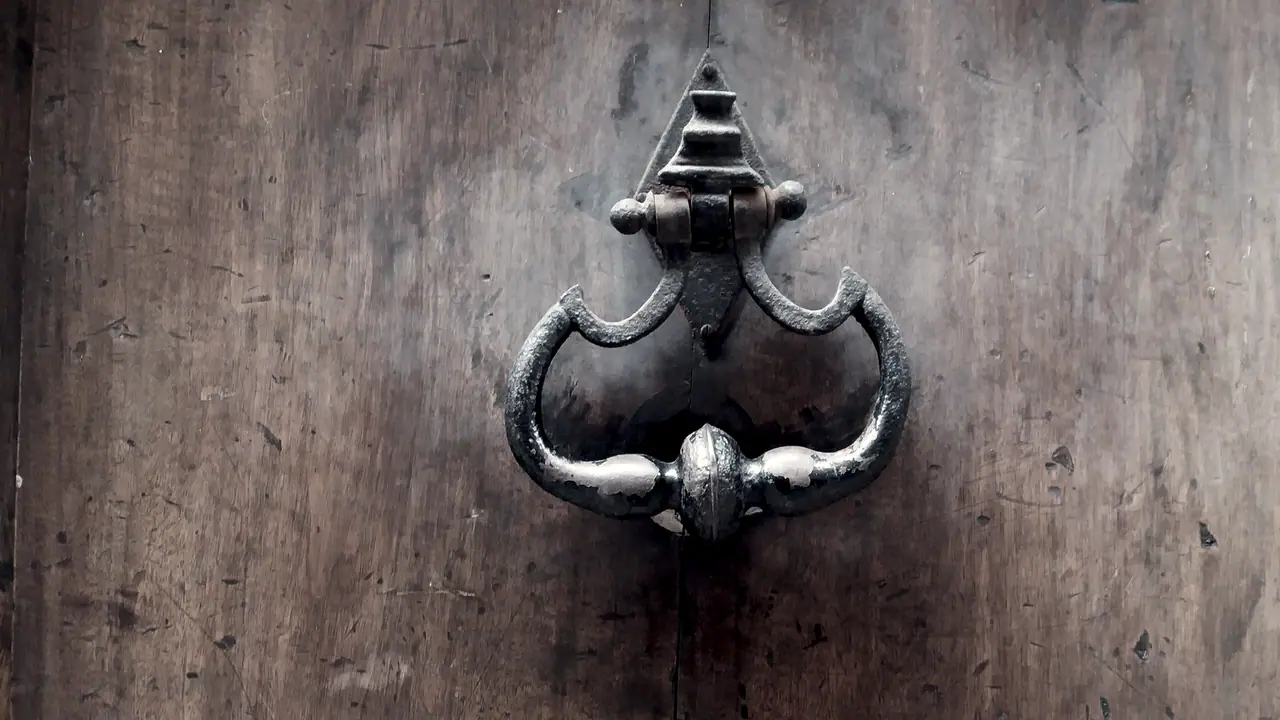 Heurtoir de fer forgé sur une porte de bois patinée de la rue Mourguet, dans le Vieux Lyon, ses branches recourbées autour d'une olive centrale.