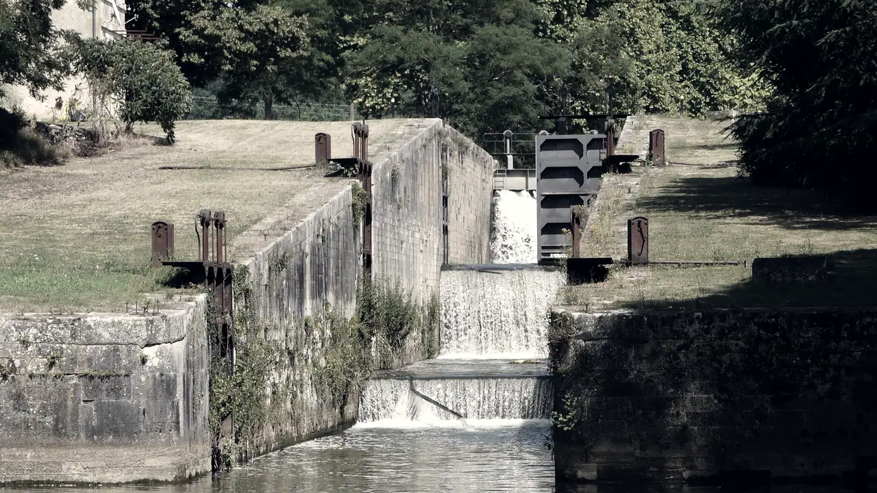 Trois écluses en escalier sur un canal : l'eau tombe en cascade d'un sas à l'autre entre des murs de pierre, depuis la porte de métal de l'écluse du haut.