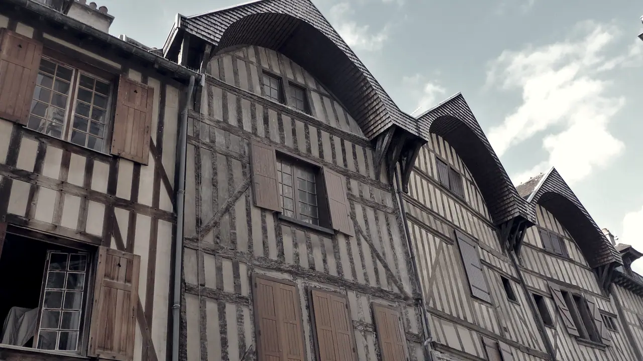 Rangée de maisons à pans de bois aux volets fermés, serrées sous leurs toits pentus le long d'une rue étroite.
