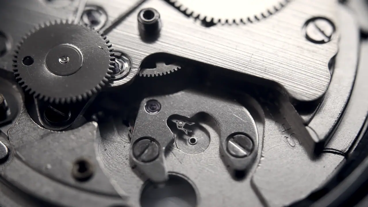 Mouvement de montre mécanique ouvert : les rouages, les vis et le balancier apparaissent sous la platine démontée.