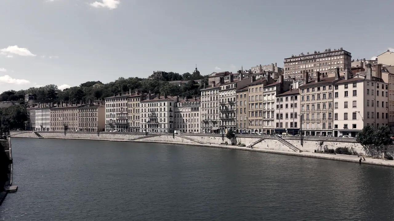 Le quai Saint-Vincent vu depuis une passerelle : une rangée d’immeubles anciens de cinq à sept étages le long de la Saône, sous la colline.