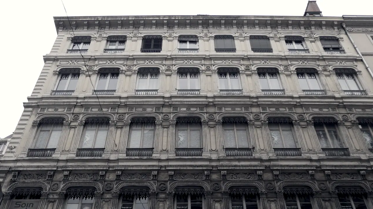 Façade d'immeuble lyonnais en pierre vue d'en bas : des étages de fenêtres régulières, encadrées de moulures sculptées, jusqu'à la corniche.