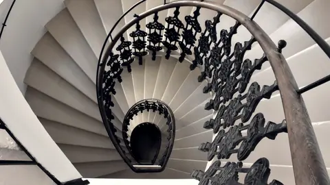 Escalier en colimaçon vu du dessus : les marches et la rampe de fer forgé s’enroulent en spirale vers le bas.