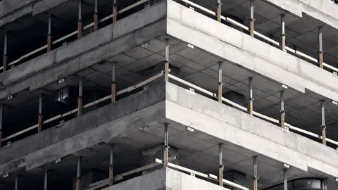 Immeuble en construction : les planchers de béton se superposent sans façade, les étages du bas déjà fermés et ceux du haut ouverts.